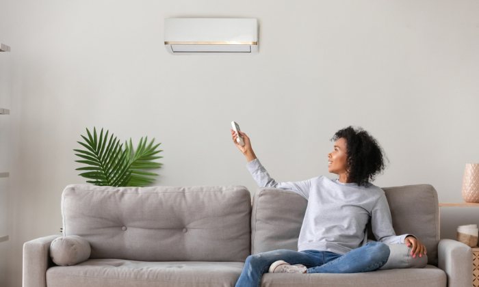 Woman on sofa turning airconditioning unit on with remote