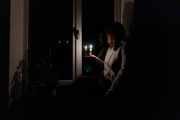 Girl with a burning candle in a dark room sits near the window