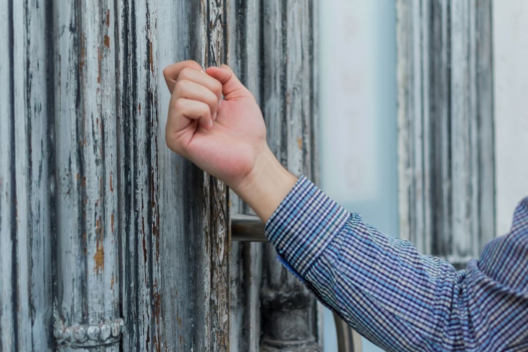 A man's hand knocks on a front door