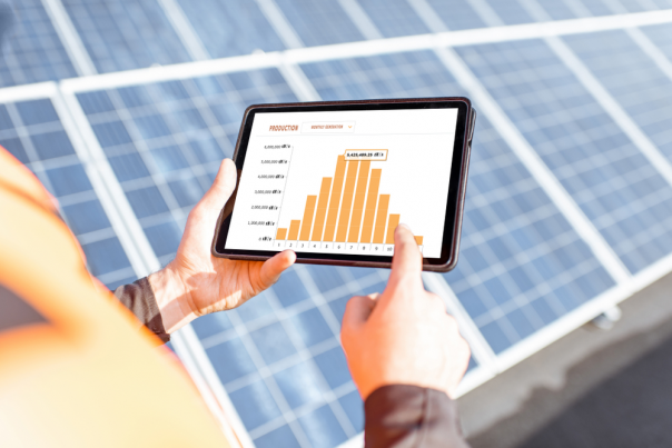 Workman examining genaration of solar power plant, holding digital tablet with a chart of electricity production.