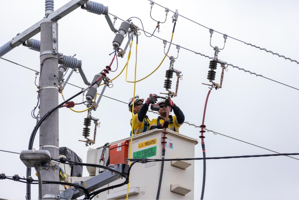 Two AusNet workers in safety gear repair transmission line from cherry picker   