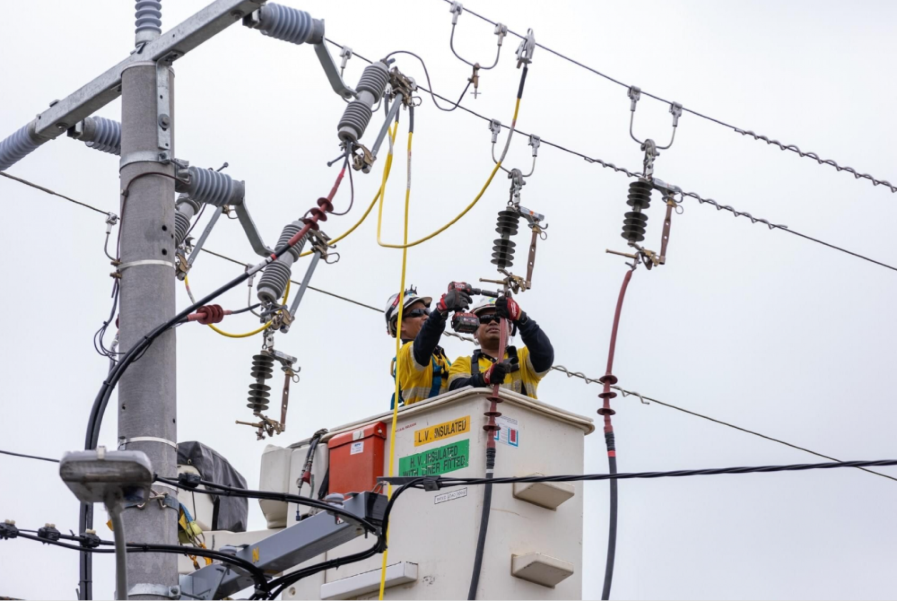 Two AusNet workers in safety gear repair transmission line from cherry picker 