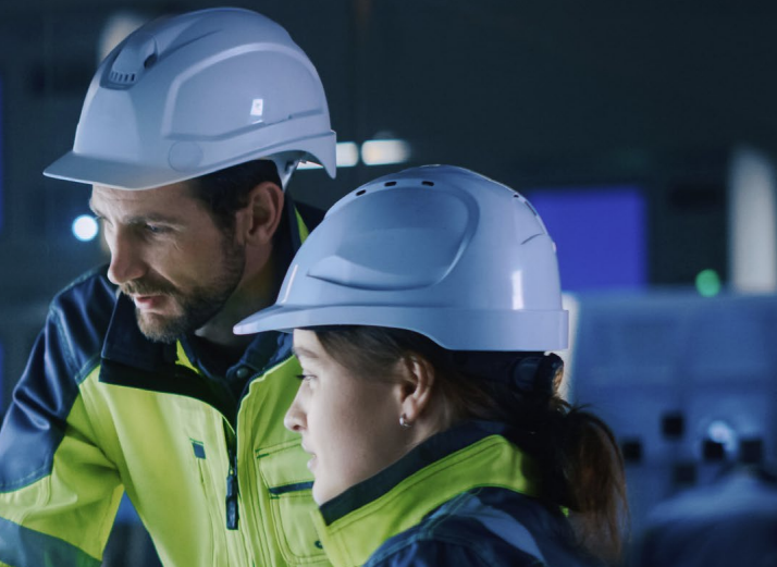 A male and female in hard hats and protective glasses observe  