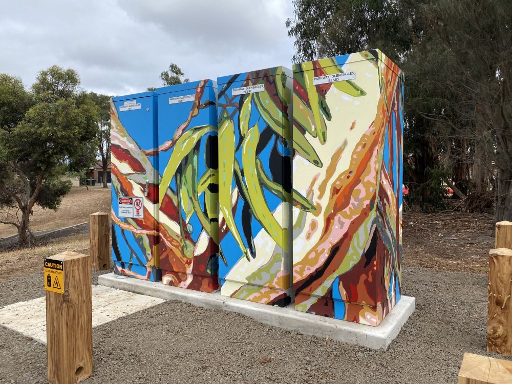 A neighbourhood battery with gum leaf mural painted on it stands in gravel setting in Tarneit  